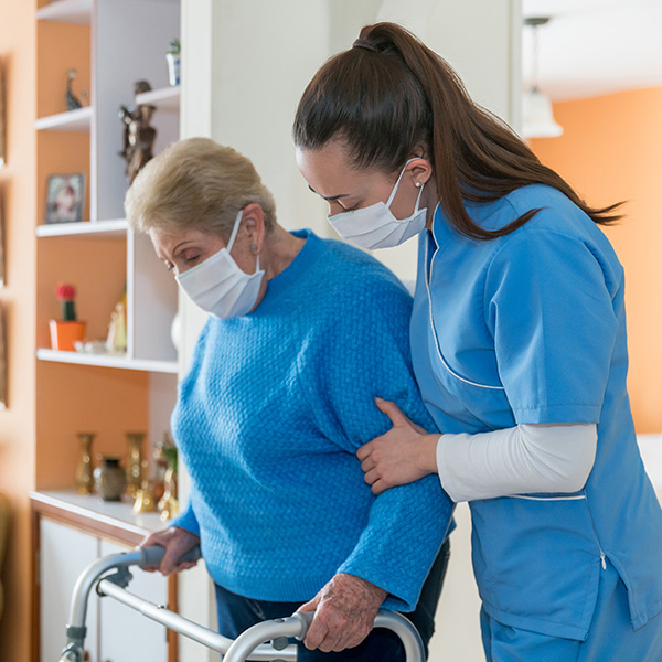 Home caregiver wearing a facemask while assisting a senior woman walking with a mobility walker