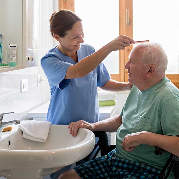 Home Caregiver with senior man in bathroom women combing elder male's hair